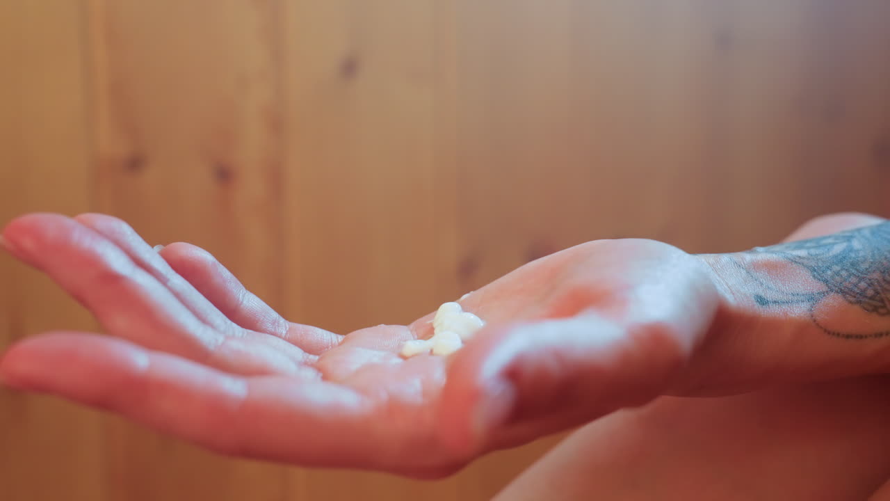 close up of white person hand with tattoo holding dab of cream in sauna wooden cabin steam rising gentle skincare ritual highlighting wellness mood and tactile care moment for skin in warm light setting