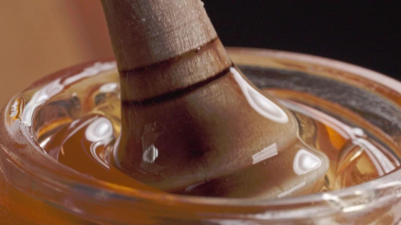 Macro ravvicinata di un mestolo per miele in legno ricoperto di denso miele dorato all'interno di un barattolo di vetro con superficie lucida e ricca consistenza naturale in Messico