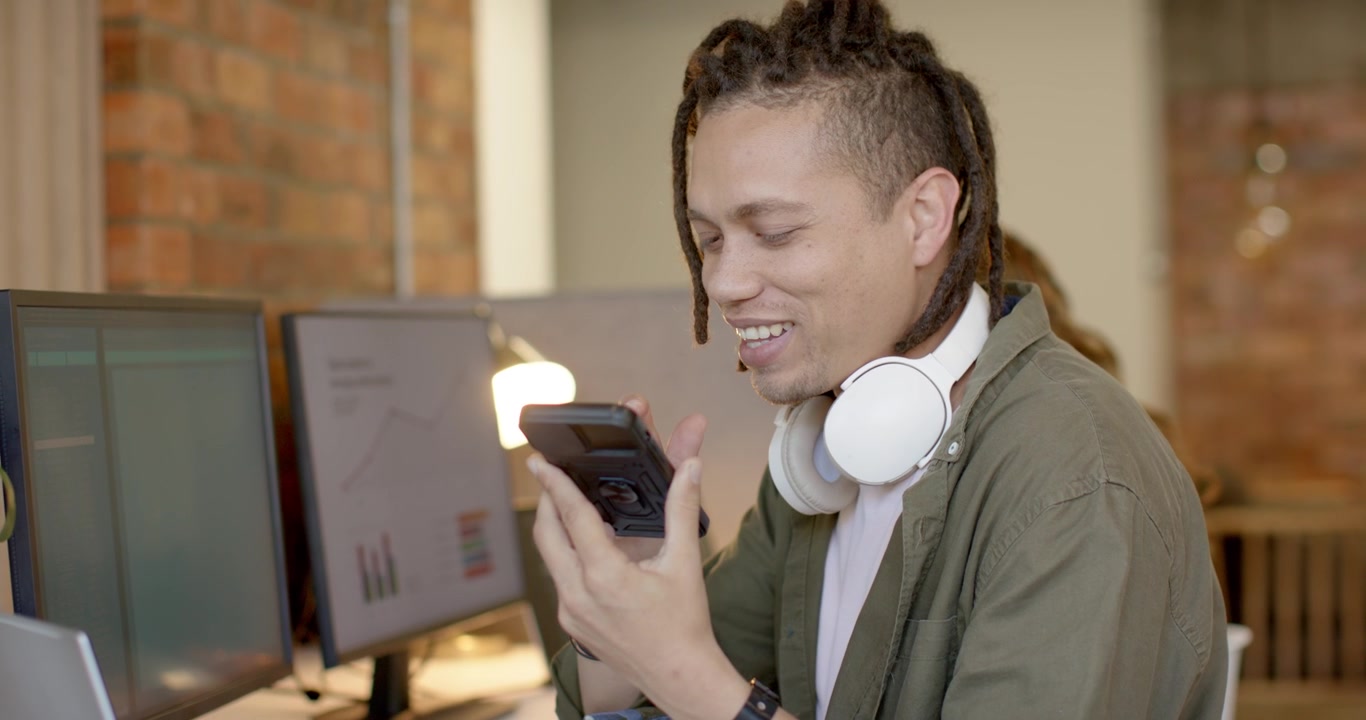African American man in olive shirt seeing phone picking it talking for update returning to laptop