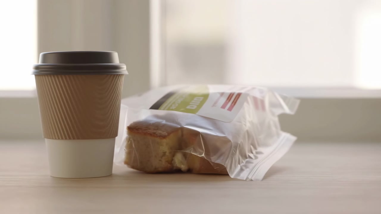 Xícara de Café e Doce Embalado em Mesa de Madeira Perto da Janela, Luz Suave da Manhã Lançando um Brilho Quente Sobre a Superfície Ondulada