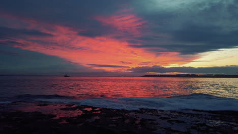 Burning-red-clouds-during-sunset-over-ocean-water-with-wave-breaking-on-shore