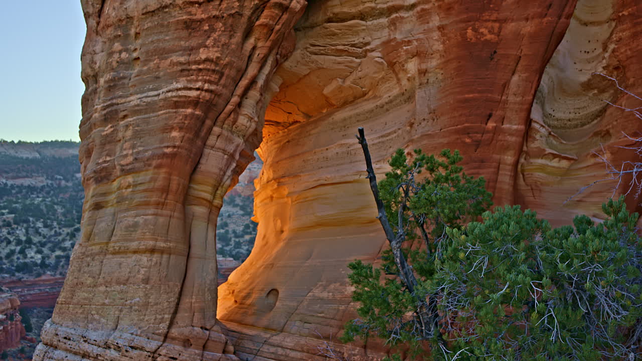 Cinematic drone view of a majestic red rock arch glowing at sunrise near Kanab, Utah.