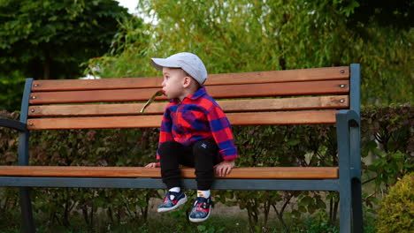 beautiful kid in cap and checkered shirt gets off the bench. toddler drinks from doy pack in the park.