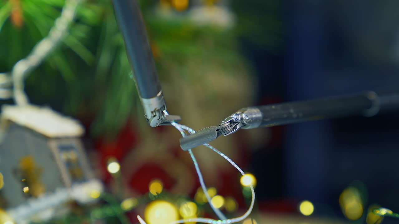 Tiny forceps of a medical surgical robot arms make a knot on the thread. Precise moves of a pair of pincers in dealing with little things close up. Christmas decorations at the background.