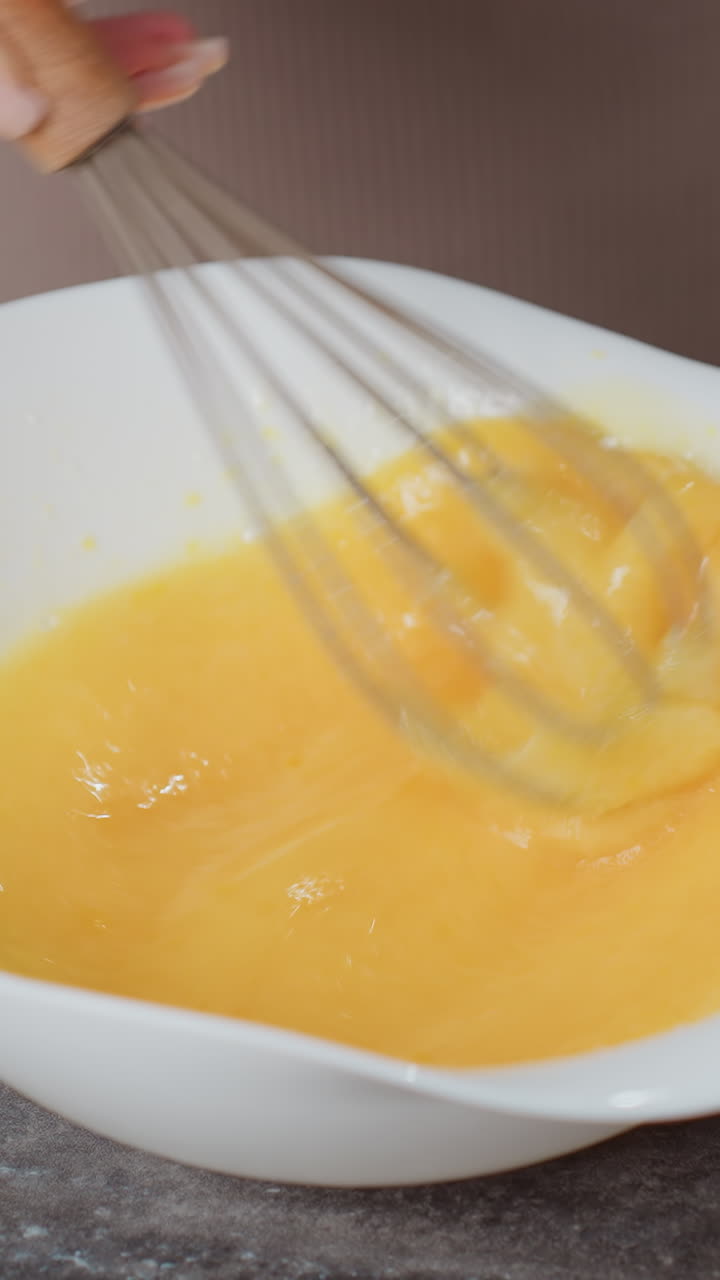 primer plano de manos golpeando huevos en un cuenco blanco en un mostrador oscuro, el borrón de movimiento captura la agitación rápida, la persona lleva ropa marrón