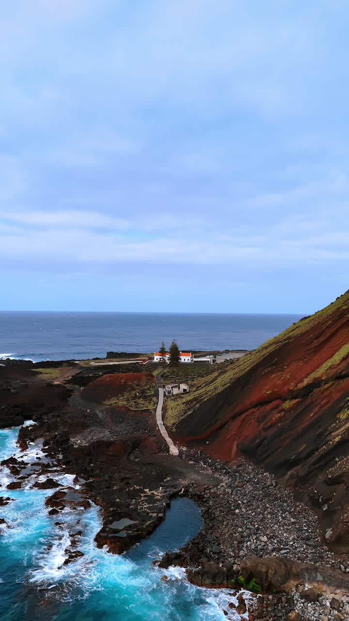 Picturesque rocky shoreline of the Azorean Islands, the Autonomous Region of the Azores. Drone flies away from the lonely house on the coast near the mountain. Vertical video.