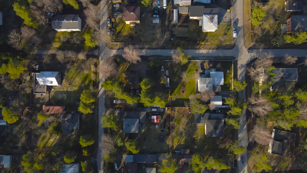 Top down aerial view flying forward and above small houses and apartment complexes in an urban area that has tall green pine trees and leafless birch trees in Laagri Estonia during a sunny day.
