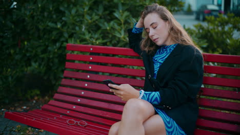 young woman sitting on a red bench using a smartphone