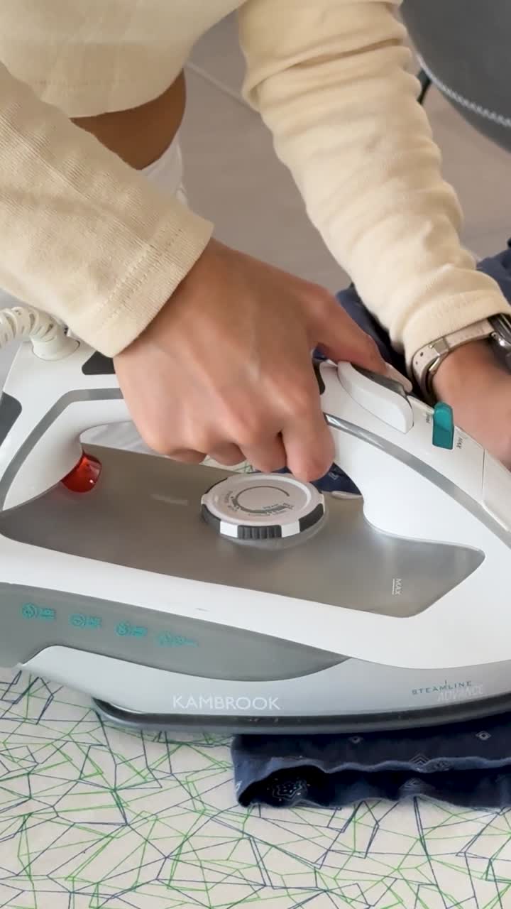 A close-up vertical shot of female hands using a steam iron on a patterned board