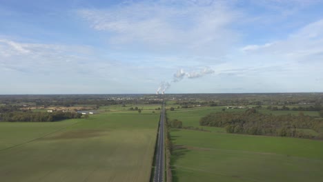 Straße-Zwischen-Grüner-Wiese-Mit-Atomkraftwerk-In-Der-Ferne,-Die-Weißen-Rauch-Ausstößt