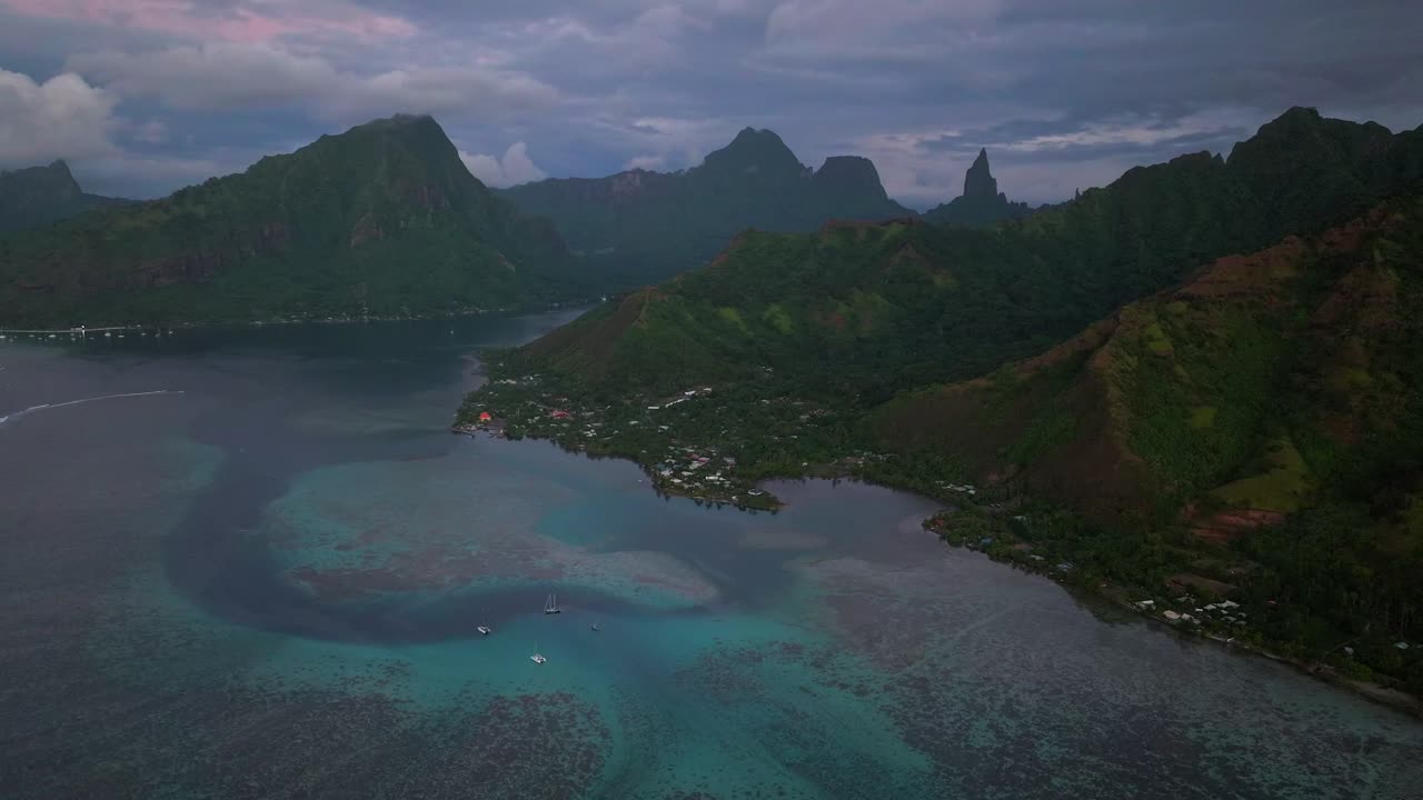 Purple sunset dusk Mount Mauaroa Tohivea Rotui Haapiti Cooks Opunohu Bay Moorea island French Polynesia aerial drone jagged mountains boats lagoon coral reef waves Pacific Ocean forward upward motion