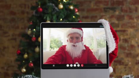 Hombre-Caucásico-Mayor-Disfrazado-De-Santa-En-Videollamada-En-Computadora,-Con-Adornos-Navideños-Y-árbol