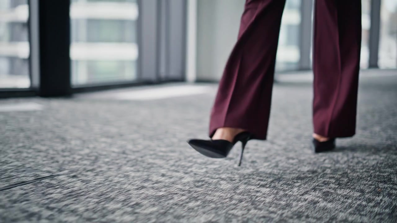 Primo piano delle gambe di una donna d'affari che cammina in ufficio con i tacchi alti. Signora in pantaloni che si muove.