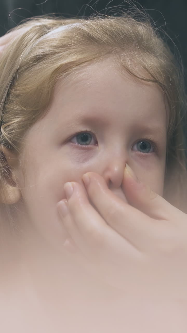 woman irrigates nose of sick little daughter with nasal spray near mirror in modern bathroom at home close view