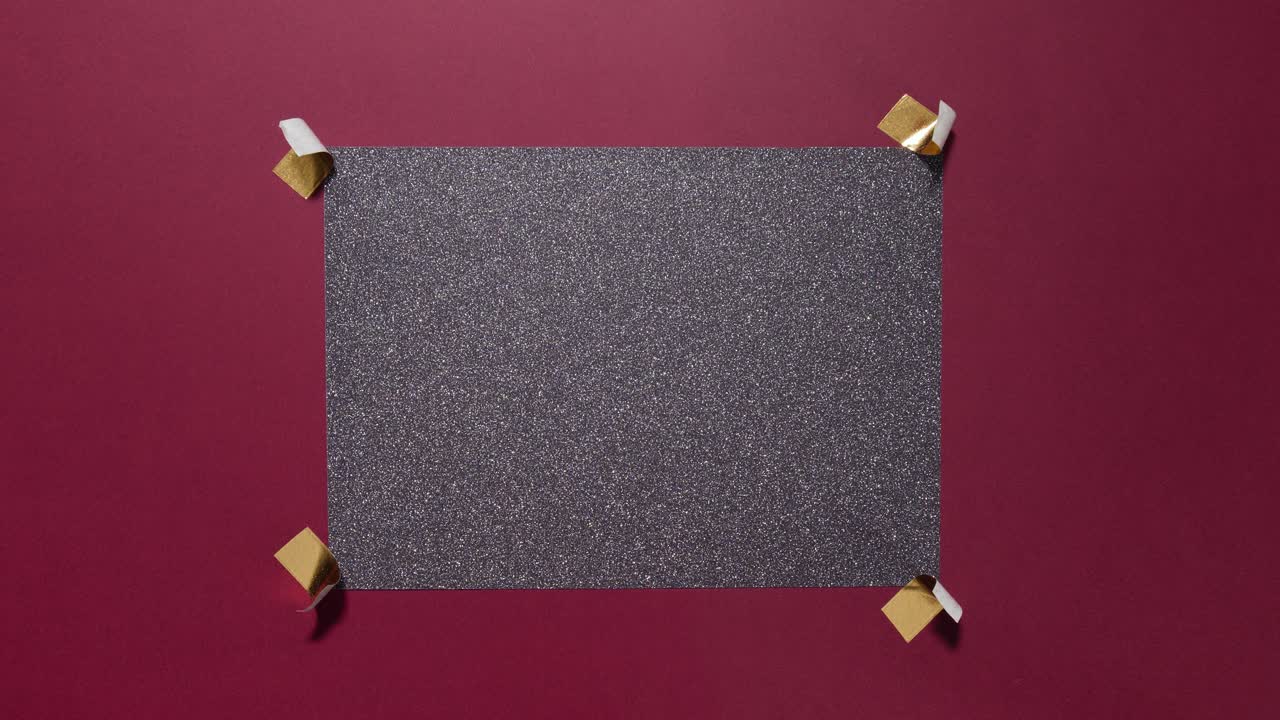 Stop motion glitter card taped with gold on a burgundy background creating copy space