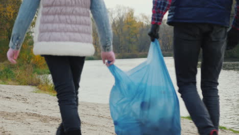 Kinder-Freiwillige-Tragen-Einen-Müllsack-Am-Ufer-Des-Sees-Entlang,-Wo-Sie-Müll-Gesammelt-Haben