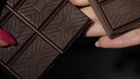 woman breaks black chocolate bar. close-up. slow motion