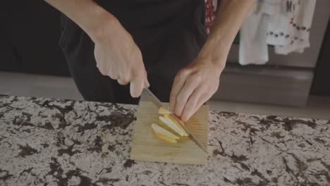 cropped view of a man slicing apple on wooden board