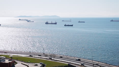 Top-view-of-Vessels,-Boats-and-Cruise-Ships-Anchored-in-Blue-Marmara-Sea-of-Istanbul-while-Cars-Passing-on-Highway-under-Open-Sky