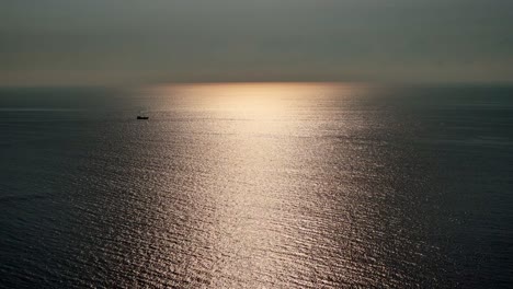 a serene ocean view captured during sunrise, with soft golden light reflecting off the calm water surface. a lone cargo ship is visible in the distance, giving a scale and to the vast seascape