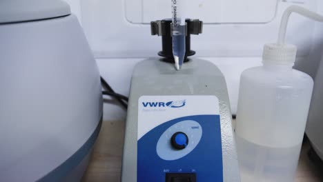 vwr mezclador de vórtice analógico se sienta en un banco de laboratorio en un laboratorio de ciencias con un solo tubo de ensayo con tapa naranja, listo para la prueba