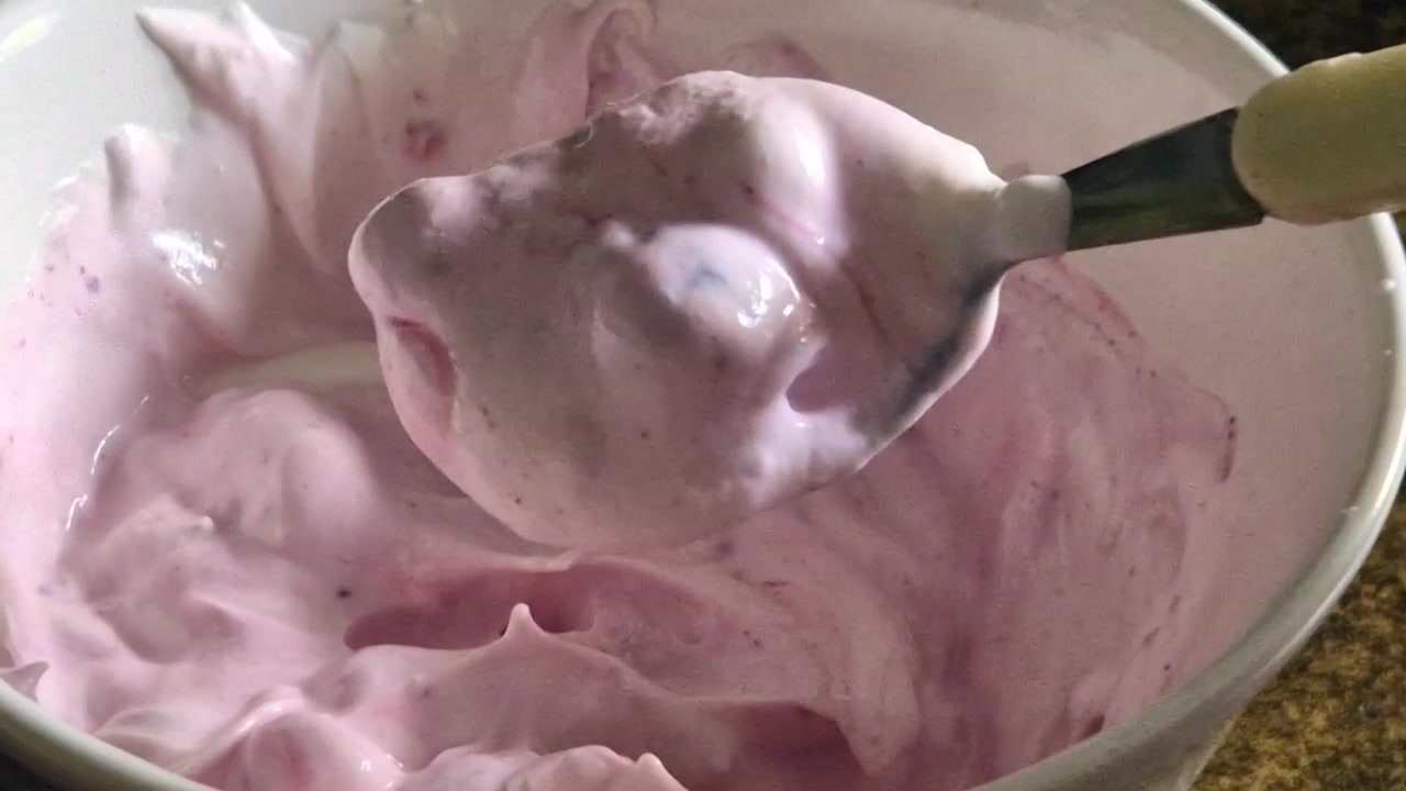 Persona che mescola con un cucchiaio yogurt greco cremoso e mirtilli per una colazione o uno spuntino sano.
