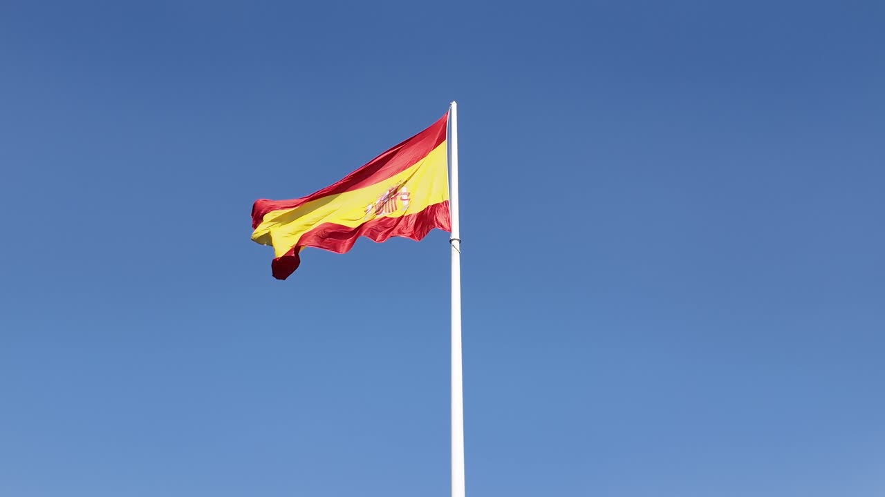 Enorme bandiera nazionale spagnola che sventola al vento su un'asta bianca in Piazza Colón, Madrid.
