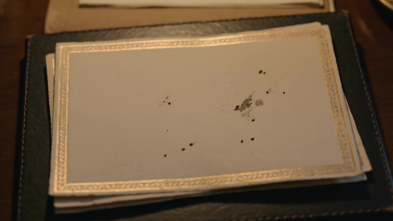 Refocusing camera bringing top card closer on folio at dining table, revealing gold border stains