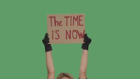 the time is now. protest text message on cardboard. stop racism. police violence. banner design concept. hands in black gloves holding a poster a green screen, chroma key. close up. slow motion