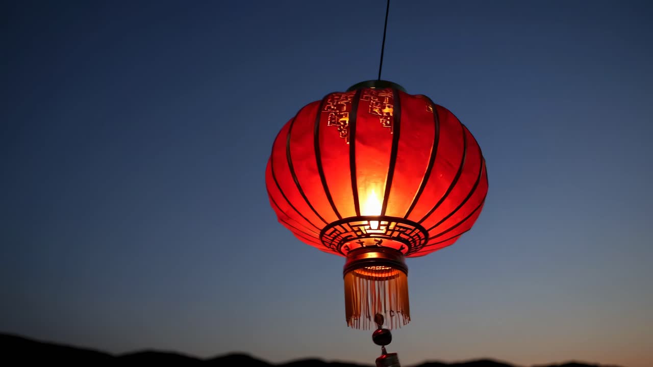 A close-up, low-angle shot of a glowing red lantern against a twilight sky, creating a serene