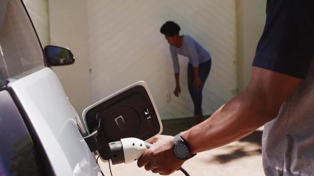 pareja afroamericana cargando un coche eléctrico en un día soleado