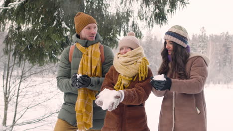 Parents-And-Daughter-Dressed-In-Winter-Clothes-Throwing-Snow-In-A-Snowy-Forest