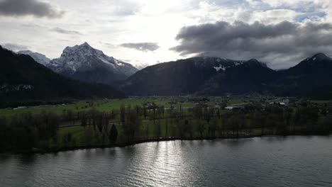 sunlight breaks between clouds with ray of light shimmering on lake and farmland fields, epic swiss mountain peaks