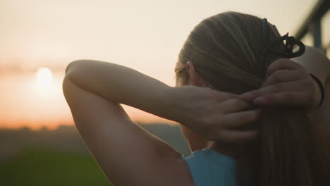 vista trasera de la joven ajustando su cabello durante el anochecer, luz suave y cálida iluminando su silueta, creando una atmósfera serena de la noche con fondo borroso y belleza natural