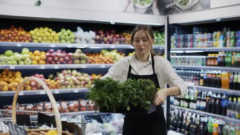 a girl worker in a black apron puts a box of greens on a shelf. work days. healthy food