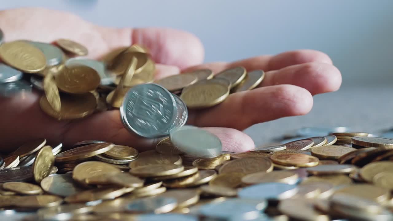 Large number of coins. Hand that holds the money. Slow motion.