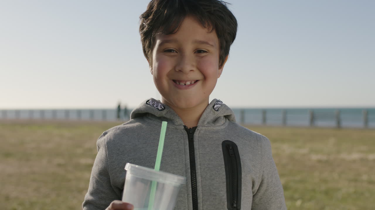 해변 공원에서 밀크 ⁇ 이크 음료를 마시는 카메라를 들고 웃는 행복한 히스패닉 소년의 초상화