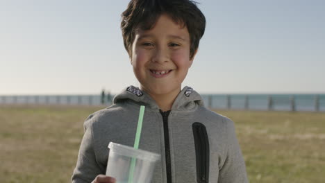 Retrato-De-Un-Niño-Hispano-Feliz-Sonriendo-Alegre-Ante-La-Cámara-Sosteniendo-Una-Bebida-De-Batido-En-El-Parque-Costero