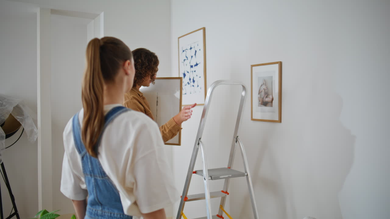 Couple arranging apartment decor hanging framed artwork on living room closeup