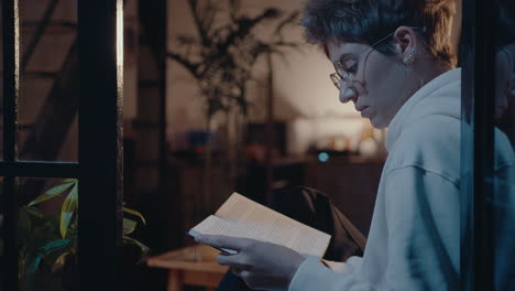 girl sitting on window sill and reading book in the evening