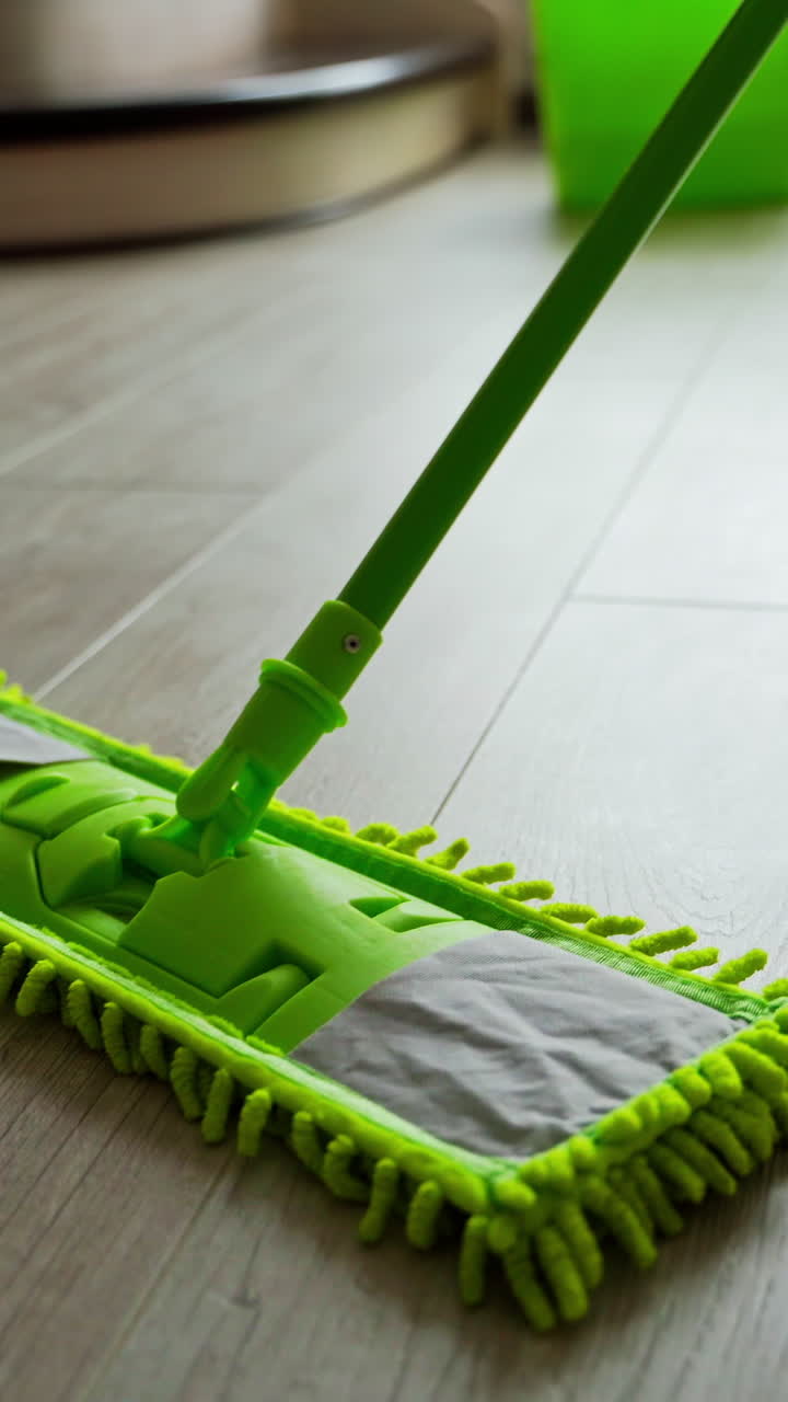 Cleaning parquet floors in the living room. Green mop cleaning the home floor. Householding duties. Close-up. Vertical video