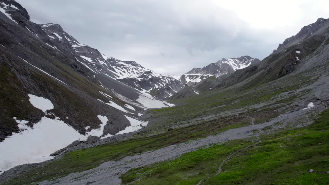 imagens de drones aéreos voando lentamente para cima e para trás para revelar uma paisagem montanhosa dramática e irregular, olhando para um cume rochoso cinza com manchas residuais de neve