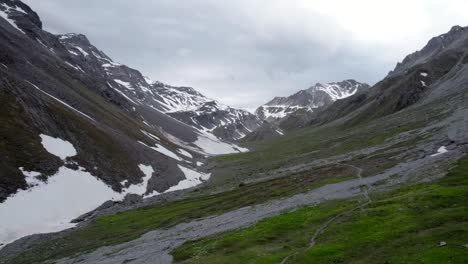 imágenes aéreas de drones que vuelan lentamente hacia arriba y hacia atrás para revelar un espectacular paisaje montañoso irregular, mirando hacia una cresta rocosa gris con parches residuales de nieve