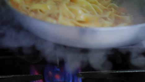 slow motion close-up of tossing tagliatelle noodles and bolognese sauce in a frying pan