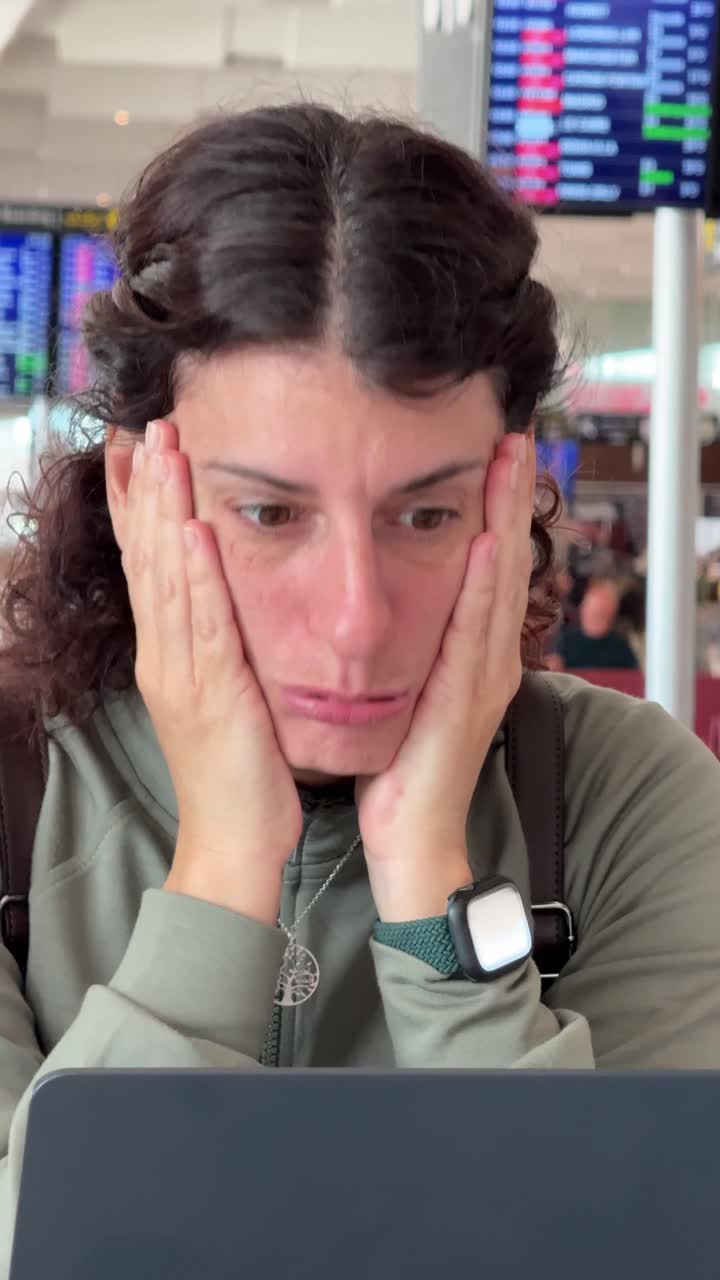 Mujer disgustada reaccionando a malas noticias en un portátil en el aeropuerto.