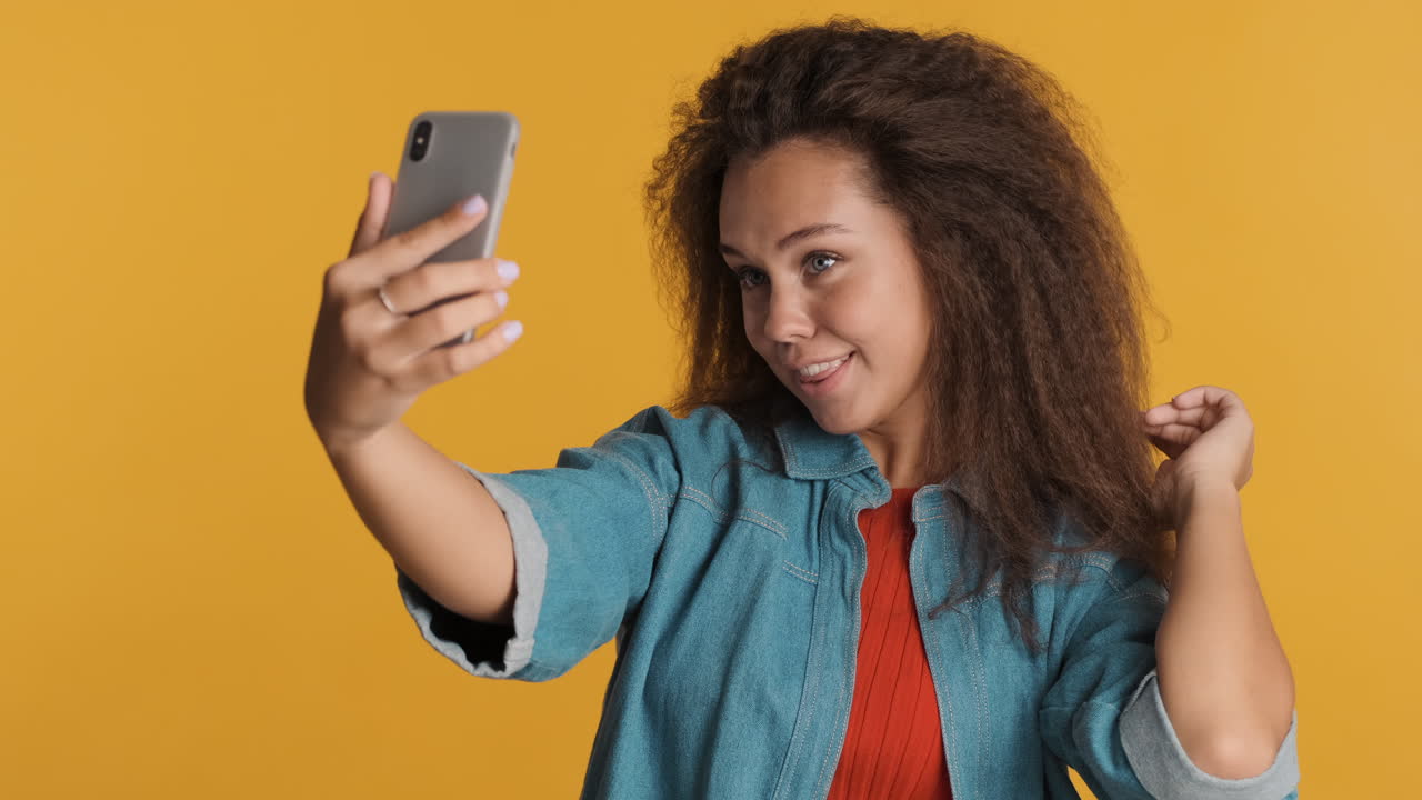 una mujer caucásica de cabello rizado tomando selfies con su teléfono inteligente.