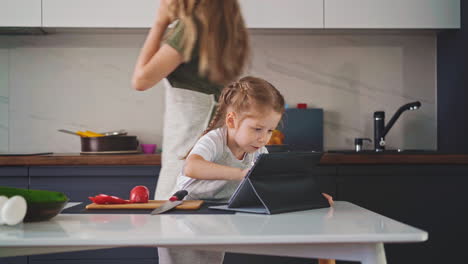 girl-looks-for-recipes-with-tablet-while-mom-talks-on-phone