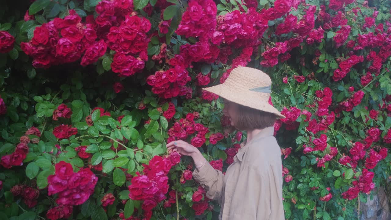 모자 를 입은 여자 정원사 가 정원 에서 자란 장미 를 새 를 맡는다