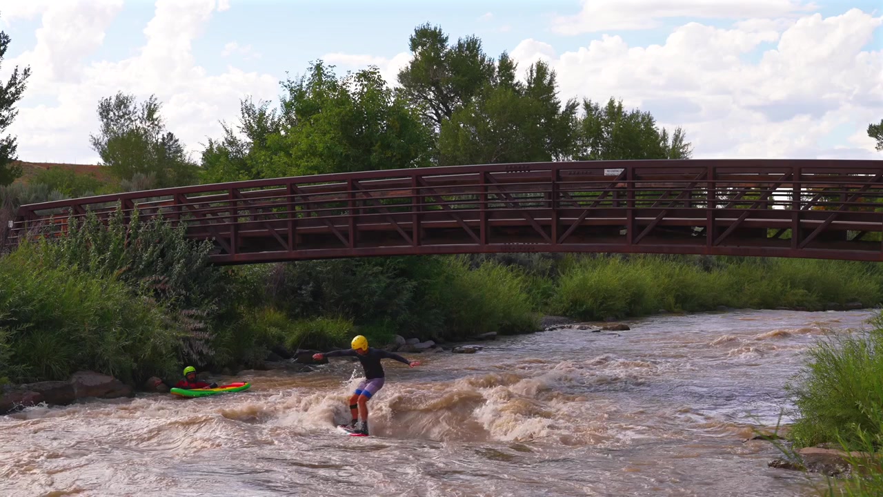 Surfisti fluviali, virate sull'onda, Parco acquatico di Montrose, Città di Montrose Colorado, Ponte del sentiero del fiume Uncompahgre, pomeriggio soleggiato, Parco Cerise, Campi McNeil, paesaggio, portata elevata, scioglimento della neve, sedimento fangoso.