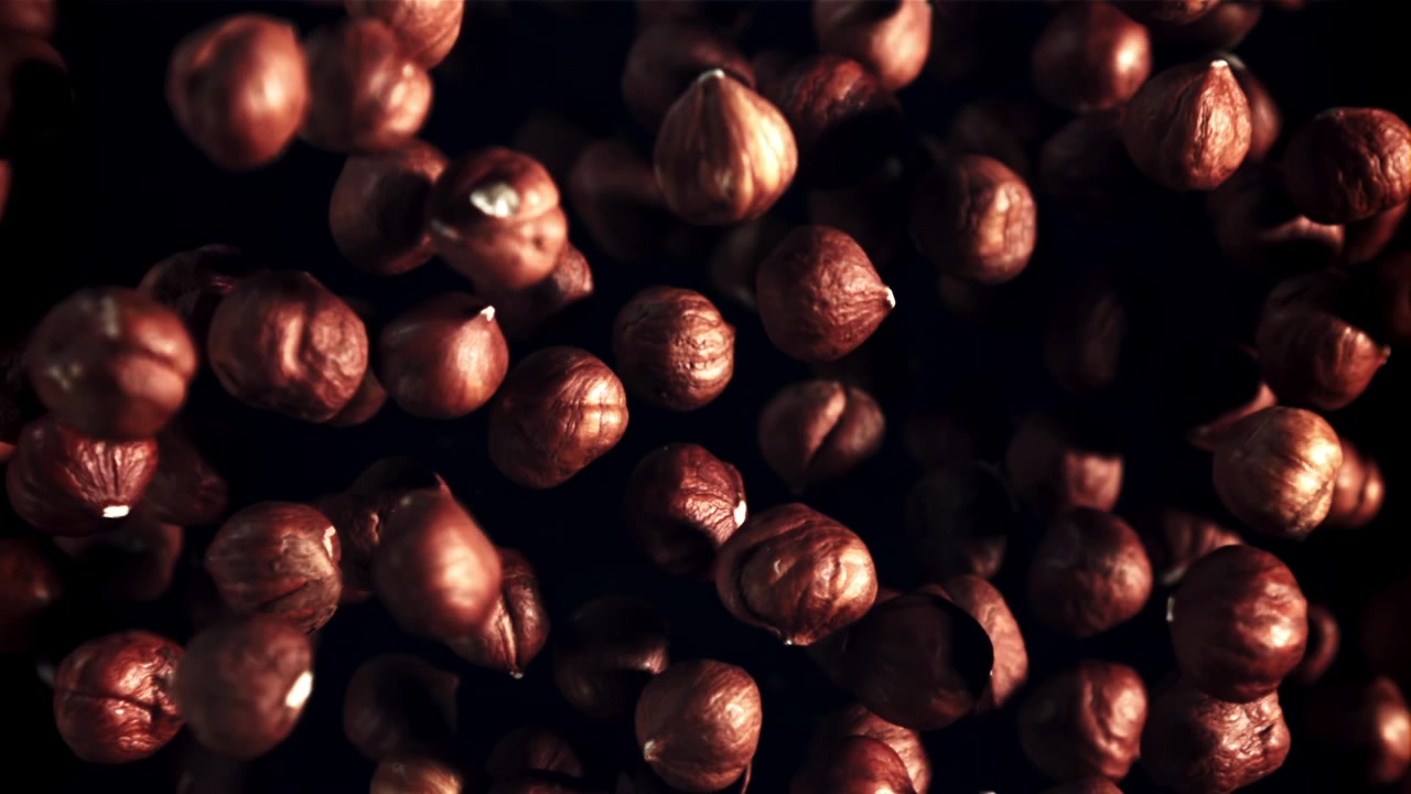 Nocciole che cadono al rallentatore su sfondo scuro.